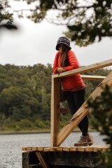 girl in a red jacket on a wooden dock that overlooks a lake surrounded by a green tunnel of plants