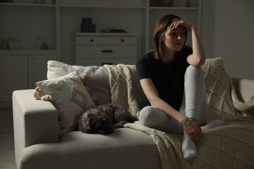 Sad young woman and her dog on sofa at home