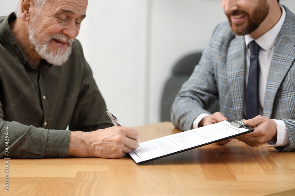 Canvas Prints Smiling notary showing senior man where to sign Last Will and Testament at wooden table indoors, closeup