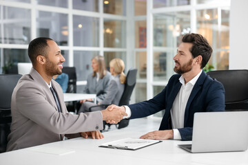 Lawyer shaking hands with client at table in office, selective focus
