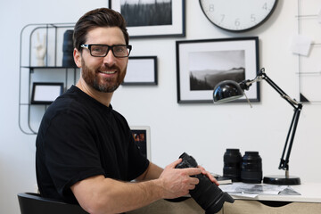 Professional photographer in glasses holding digital camera at table in office