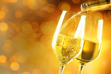 Pouring white wine into glass against golden background with blurred lights, closeup. Space for text