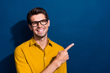 Photo portrait of nice young male point empty space specs dressed stylish yellow garment isolated on dark blue color background