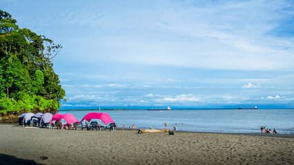 Fototapeta na wymiar Beach sea and sun resting under fuchsia and blue sunshades