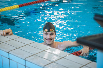 Portrait of a young professional athlete, a swimmer with a black swimming cap looking at the camera with goggles