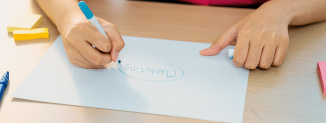 A cropped image of female businesswoman hand writing marketing on paper with pencil and sticky...
