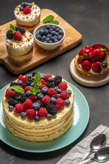 Homemade cake with fresh berries and sweet desserts on dark background.