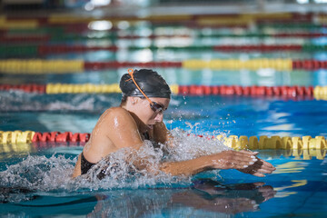 Female athlete swimming in breaststroke style in the pool lane, stroking, immersing, and lifting...
