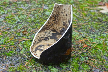one sharp dangerous fragment of a broken ceramic large dirty old home flower vase with black patterns stands  on the ground on the street during the day