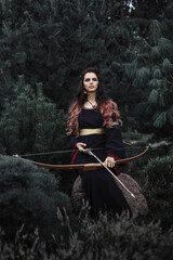 Beautiful dark elf princess in the forest. Fantasy witch with bow and arrow.