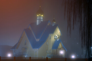 Orthodox Church at foggy and warm winter night in february Salaspils Latvija. The blue roof and golden dome with cross glowingin reflecting street lantern lights. Dark background.