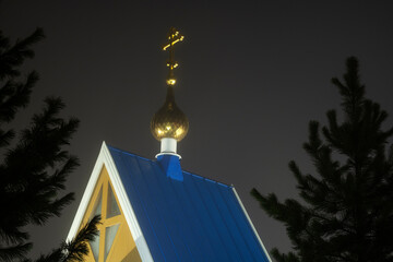 Orthodox small Church at foggy and warm winter night in february Salaspils Latvija. The blue roof and golden dome with cross glowingin reflecting street lantern lights. Dark background.