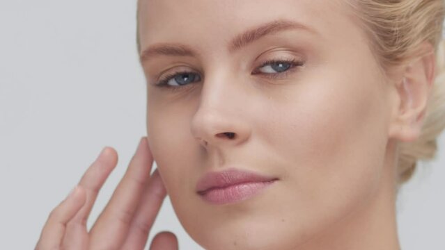 Studio portrait of young, beautiful and natural blond woman applying skin care cream. Face lifting, cosmetics and make-up concept.