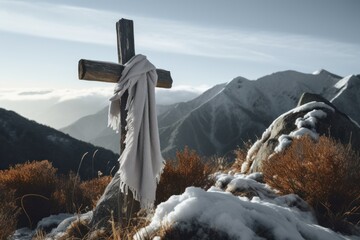 White silk scarf blowing in the wind on a wooden cross overlooking a valley between mountain peaks at sunset.