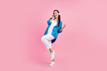 Full size photo of overjoyed nice girl dressed blue shirt white trousers sing song in headphones isolated on pink color background