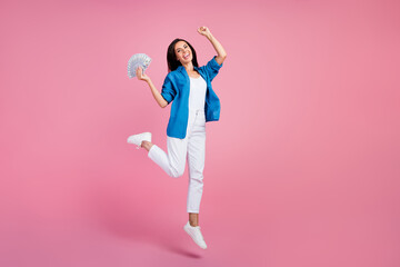 Full length photo of ecstatic overjoyed woman wear stylish shirt white pants jumping hold money win...