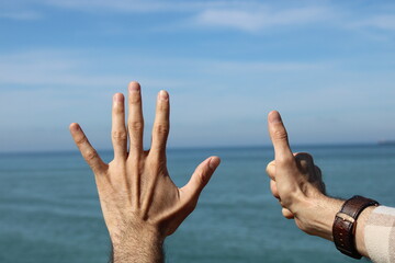 Hand doing,showing number gesture symbol six on blue summer sky nature background. Gesturing number...