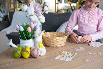 A cute girl with pink bunny ears makes an Easter craft - decorates an egg in the form of a unicorn...
