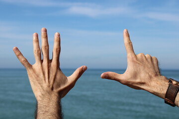 Hand doing,showing number gesture symbol seven on blue summer sky nature background. Gesturing...
