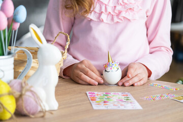 A cute girl with pink bunny ears makes an Easter craft - decorates an egg in the form of a unicorn...