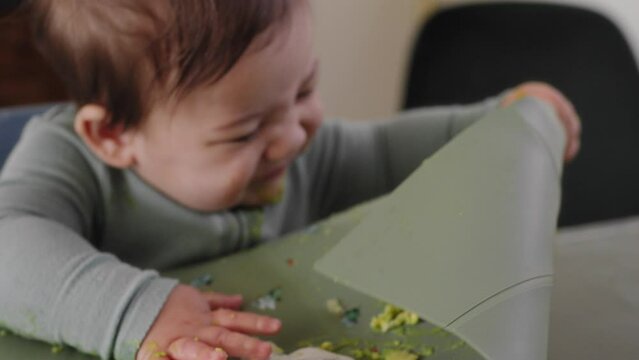 Baby boy covered in avocado plays with his placemat