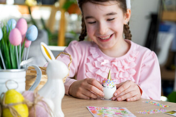 A cute girl with pink bunny ears makes an Easter craft - decorates an egg in the form of a unicorn...