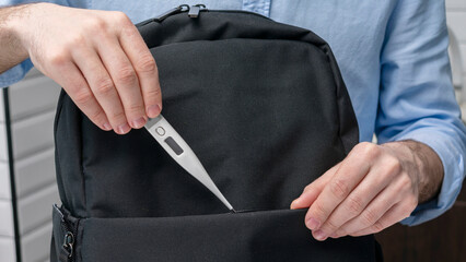 Man takes an electronic thermometer with him on the road, puts the thermometer in a backpack, male hands, cropped image, close-up, 16:9