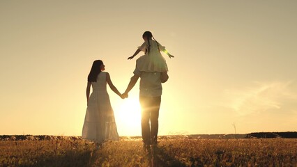 Father and wife strolling with daughter atop shoulders and silhouettes blending into sky in...