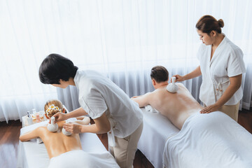 Hot herbal ball spa massage body treatment, masseur gently compresses herb bag on couple customer...
