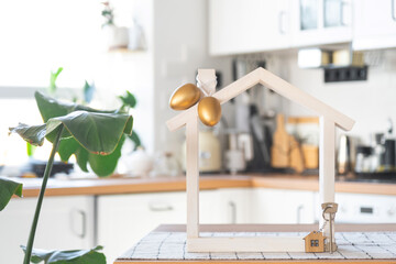 Key and tiny house of cozy home with Easter decor with color eggs on table of kitchen. Building, design, project, moving to new house, mortgage, insurance, rent and purchase real estate - obrazy, fototapety, plakaty