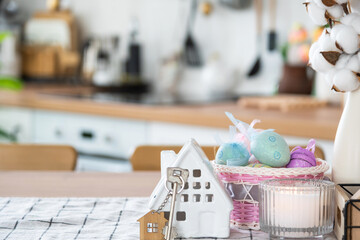 Key and tiny house of cozy home with Easter decor with color eggs on table of kitchen. Building, design, project, moving to new house, mortgage, insurance, rent and purchase real estate