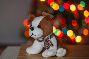 A plush dog on the background of a Christmas tree decorated with colorful Christmas garlands. There...