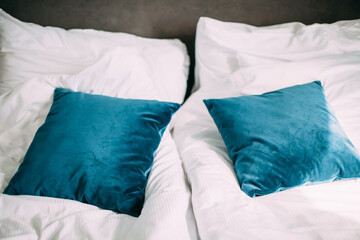 Fototapeta na wymiar Two blue velvet decorative pillows lie on white bed linen on the bed in the hotel room