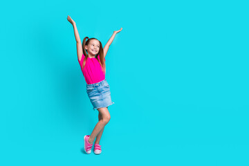 Photo of cheerful optimistic lovely girl wearing stylish outfit with hands up looking empty space isolated on cyan color background