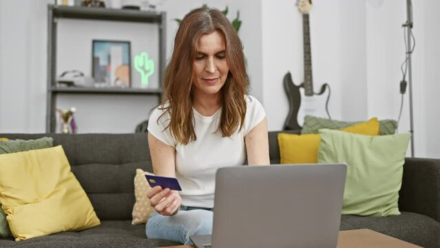 Mature woman shopping online with credit card and laptop in living room