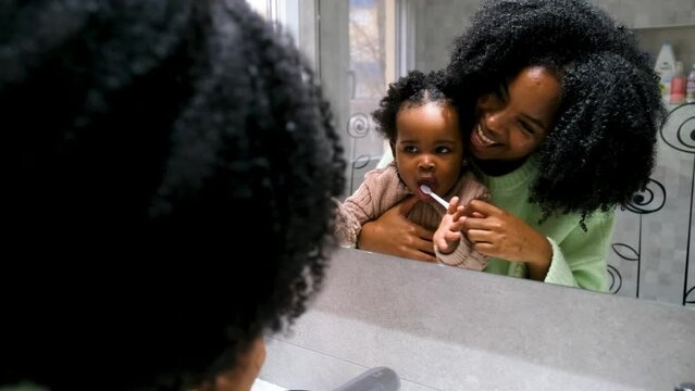 Cuban mother brushing her toddler daughter's teeth with toothbrush in the bathroom.