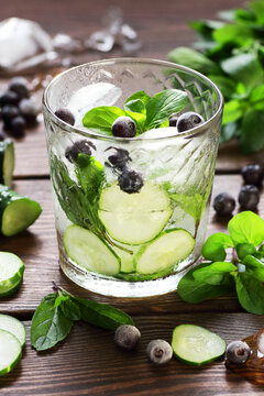 Cucumber and blueberry flavored with mint water or alcohol tonic cocktail on wooden table on dark background, vertical, fresh spring and summer detox drinks, natural healthy food concept