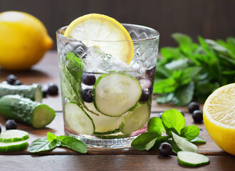 Cucumber and blueberry flavored with mint water or alcohol tonic cocktail on wooden table on dark...