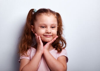 Oops. Fun positive smiling kid girl looking holding the hands near the face on empty copy space studio blue background. Closeup