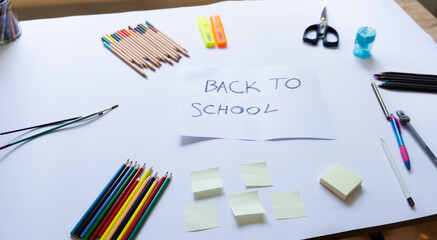 School accessories on a white background and white paper in the middle with "back to school' text on it. View from above, top view. Concept for back to school, School supplies. Copy space