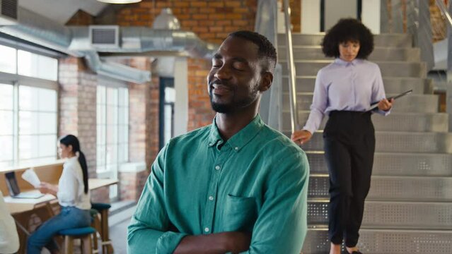 Portrait of businessman with serious expression working in modern open plan office turning to look at camera and folding arms with colleagues in background - shot in slow motion