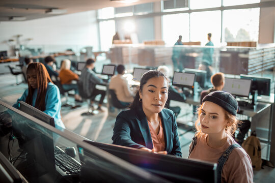 Female professor helping student on computer at college library
