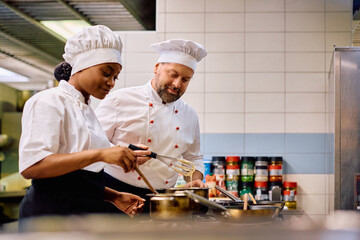 Mature chef and his black female colleague cooking together in kitchen in restaurant.