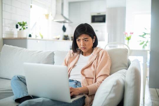 Woman looking concerned while using laptop on couch