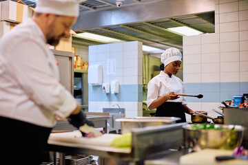 Fototapeta na wymiar Young black female cook preparing meal while working in restaurant.