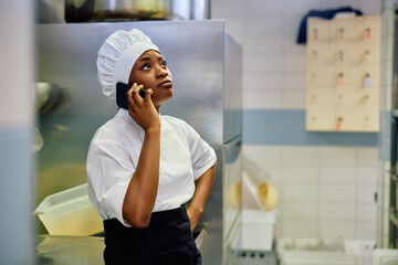 Distraught black female chef making  phone call while working in kitchen.