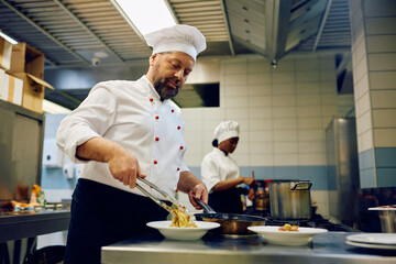 Mature cook serving dish in restaurant kitchen.