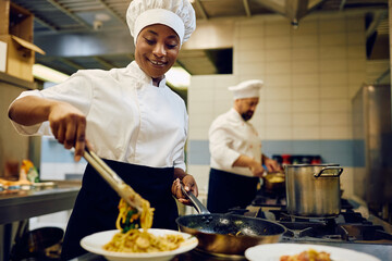 Happy black female chef serving food while working in restaurant kitchen.