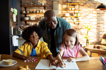Grandfather helping children with homework at home - obrazy, fototapety, plakaty