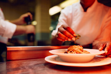 Close up of black professional cook serving dish in restaurant.